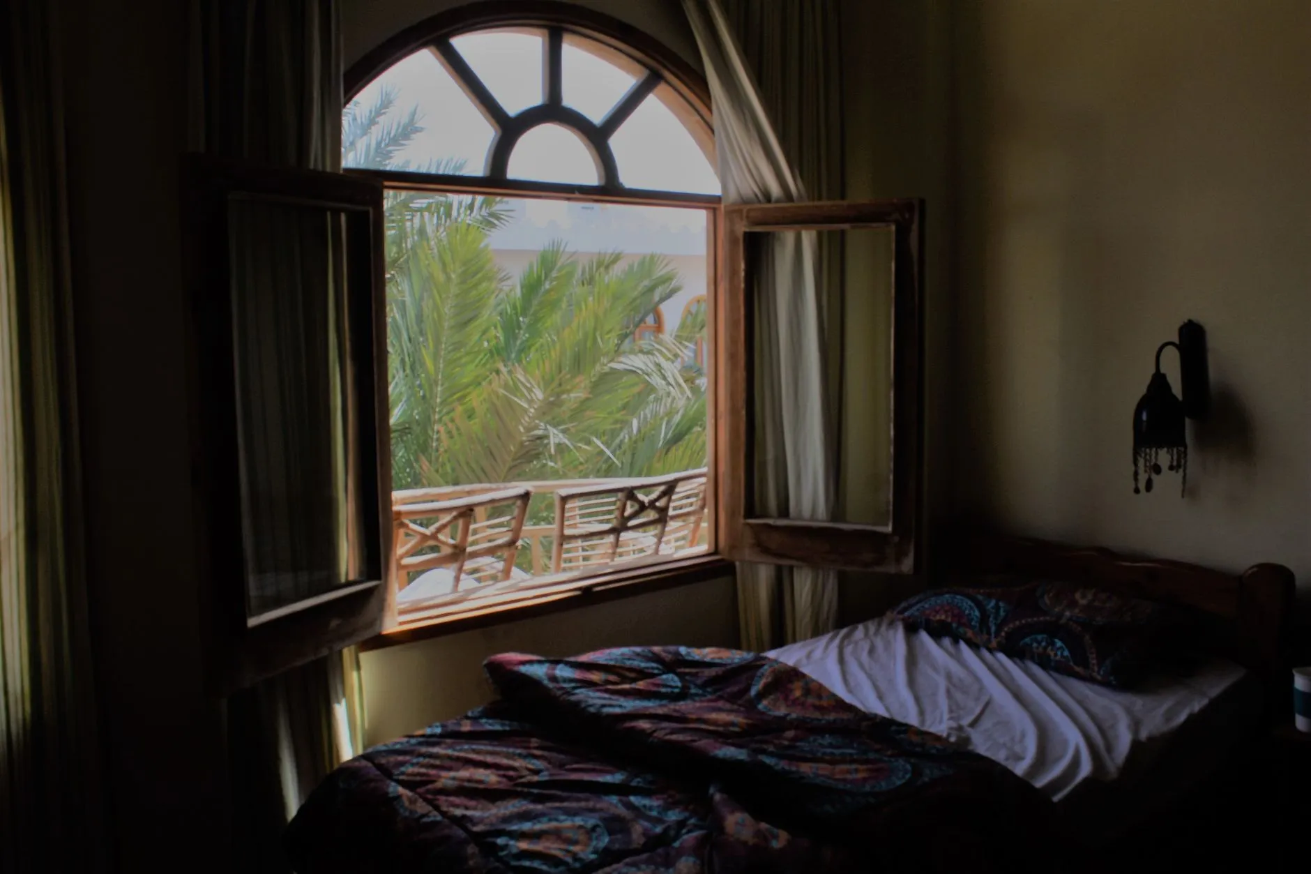 Chambre avec une fenêtre ouverte donnant sur des palmiers, dans un climat chaud